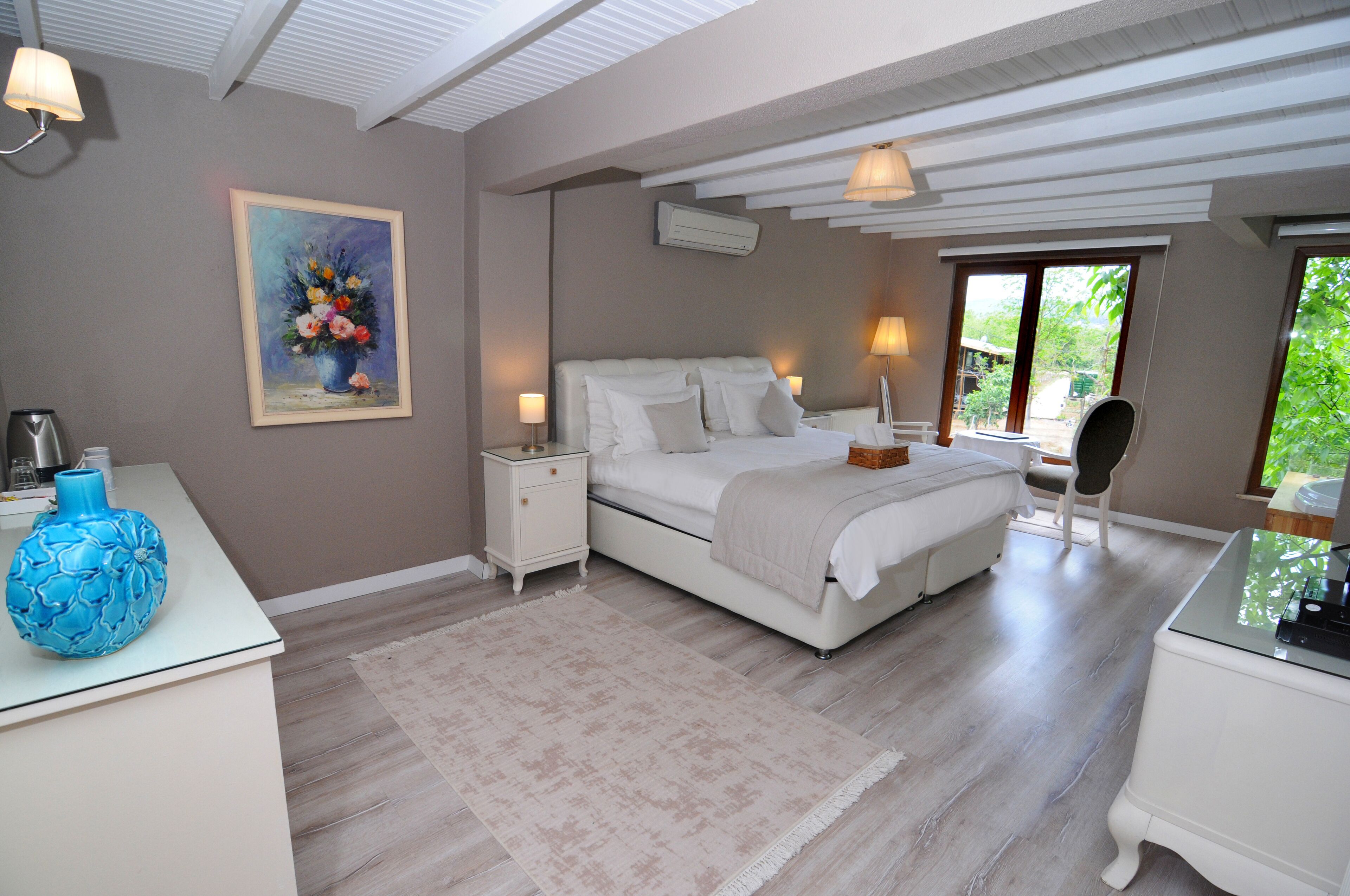 Un dormitorio con cama, mesitas de noche, lámpara, un jarrón y un cuadro en la pared.