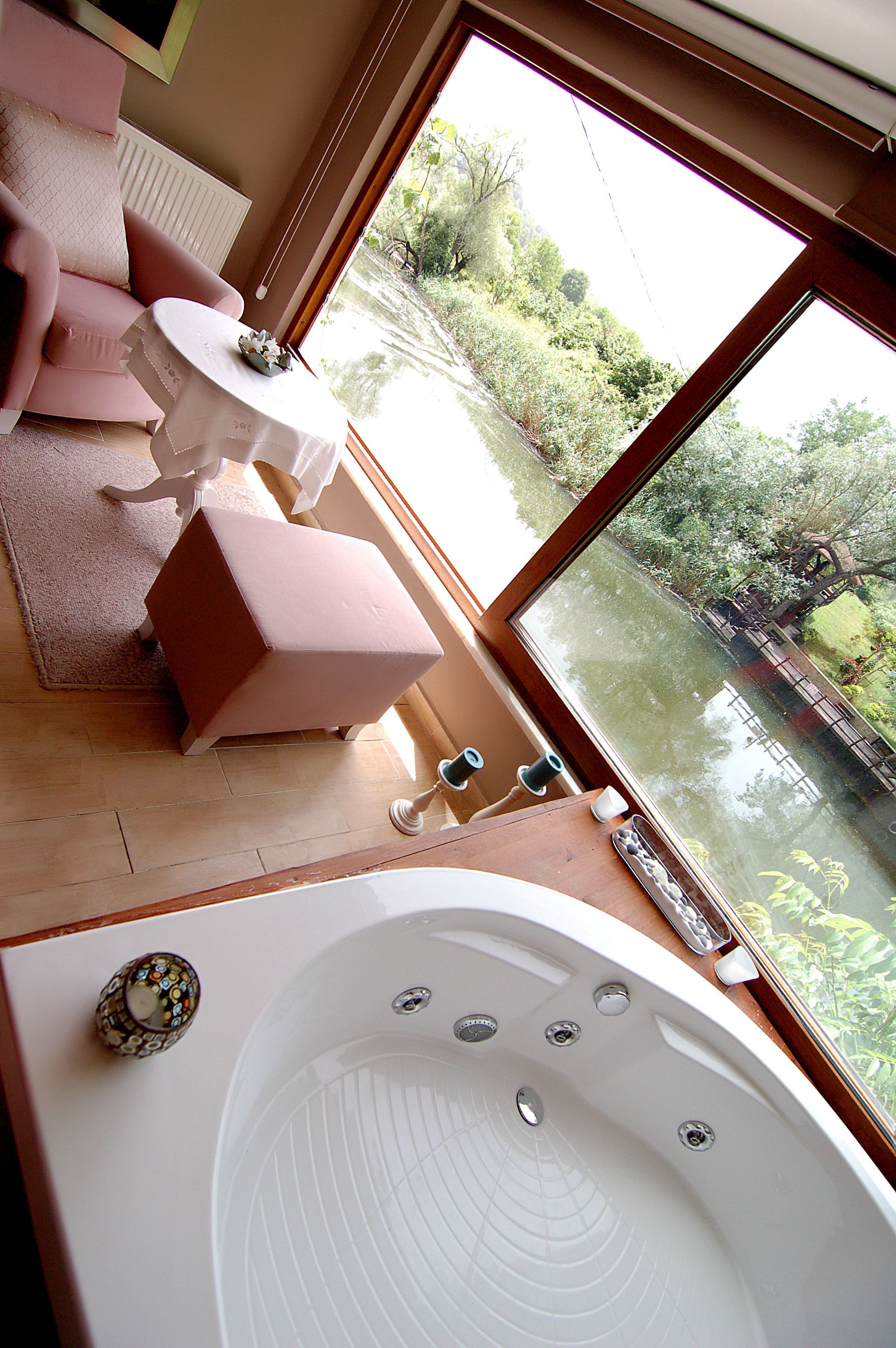 A room with a large bathtub, a pink sofa, and a table with a flower vase.