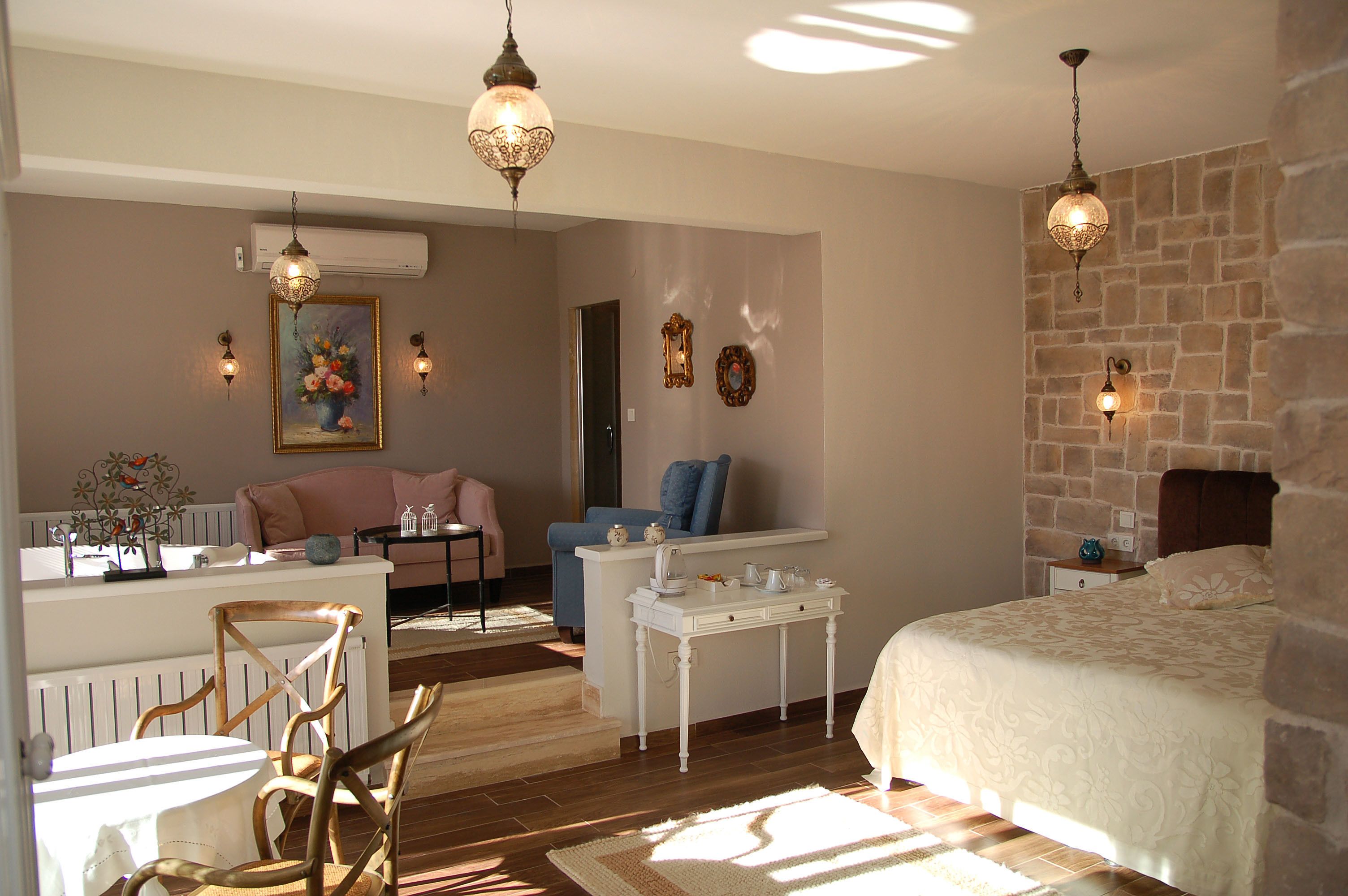 Une chambre confortable avec un grand lit, une petite table, une chaise et un bureau. Un tableau orne le mur et une fenêtre laisse entrer la lumière naturelle.