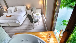 Habitación de hotel con cama, una silla, una mesita, bañera y vistas a un cuerpo de agua.