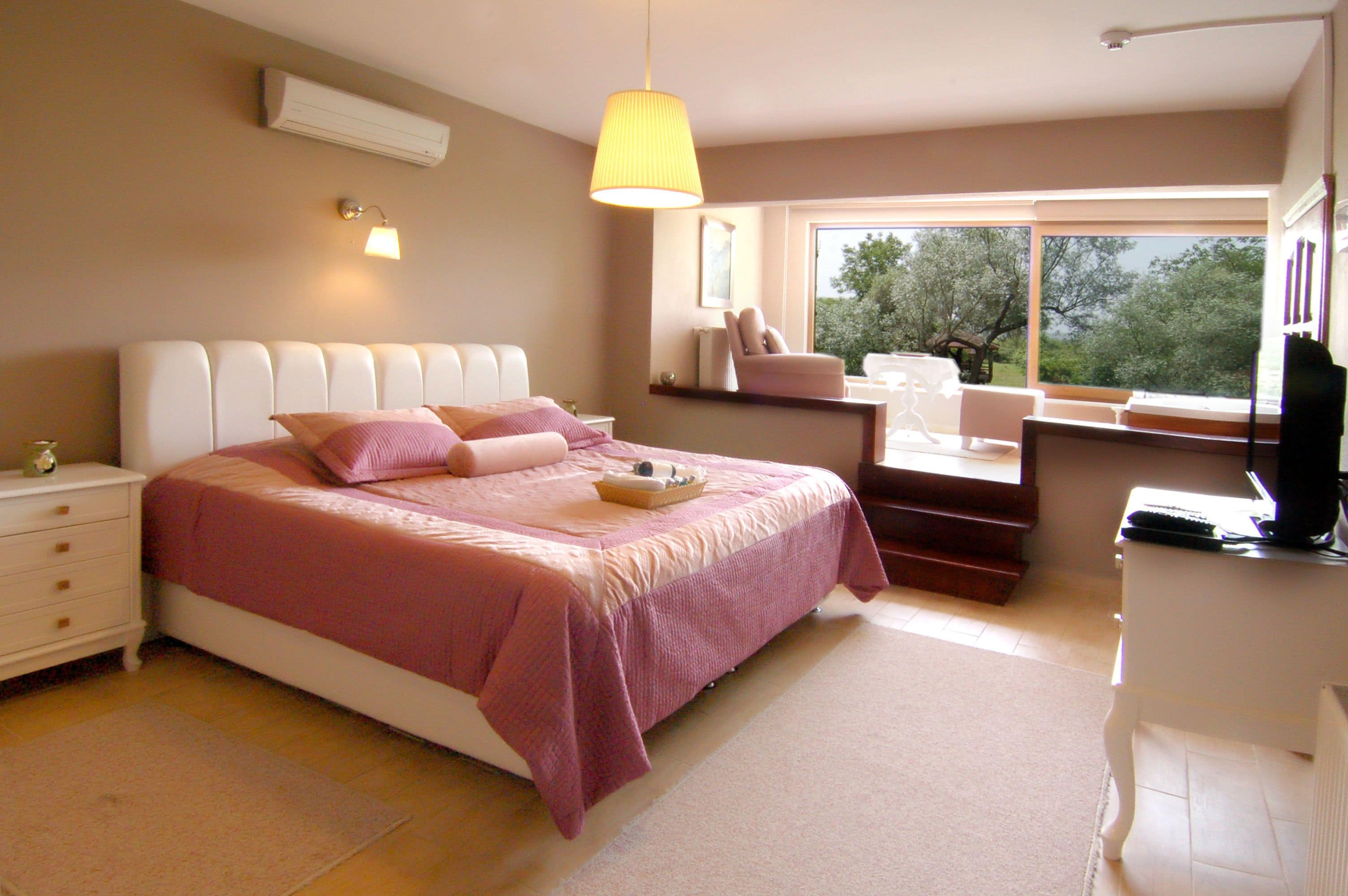 Un dormitorio con cama, mesita de noche, lámpara y ventana con vista a árboles.