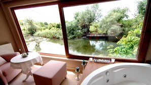 Una habitación con un ventanal grande, una bañera, un sofá rosa, una mesita y un banco.