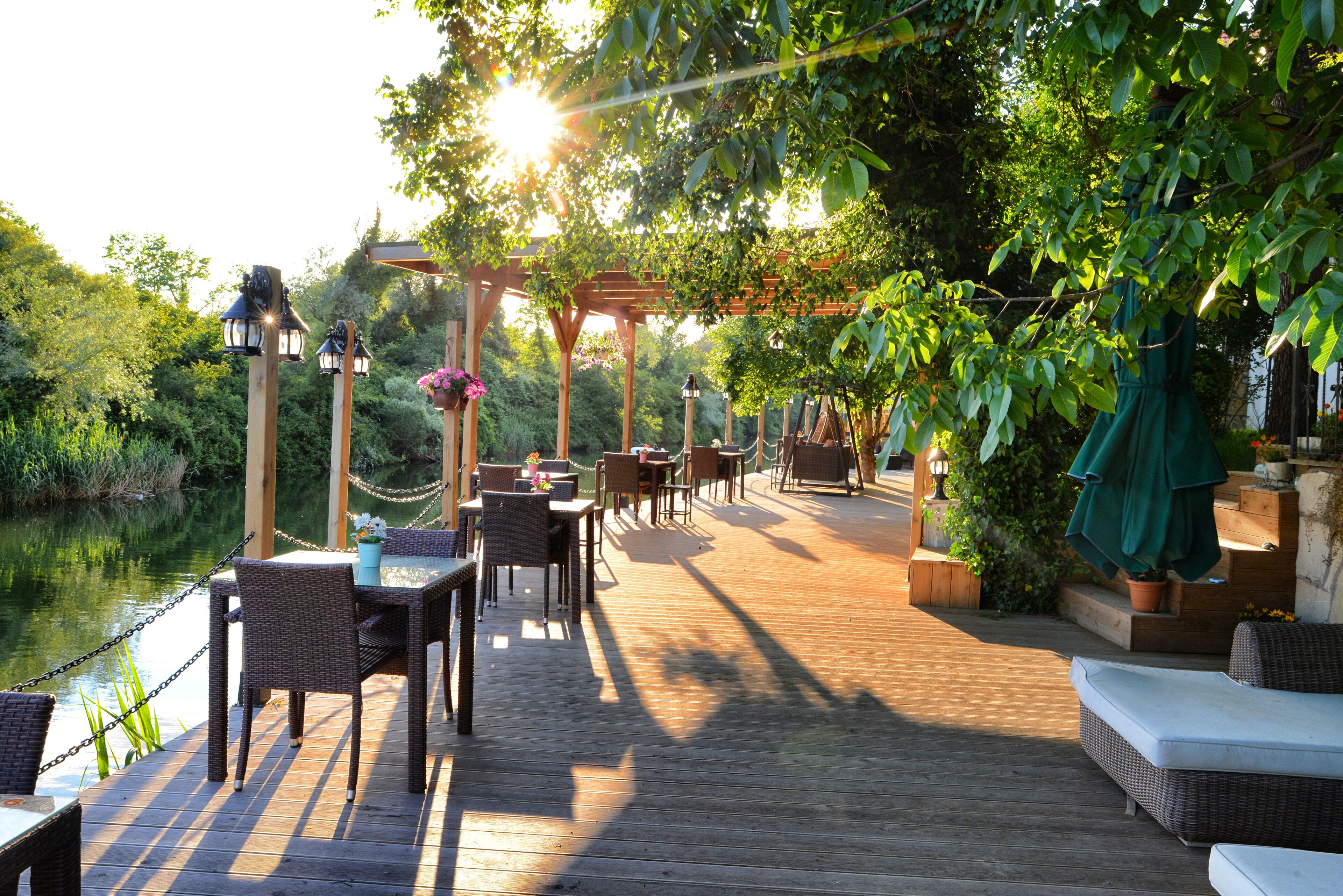 Une terrasse en bois avec des sièges extérieurs, entourée de verdure et bordée par un plan d’eau.