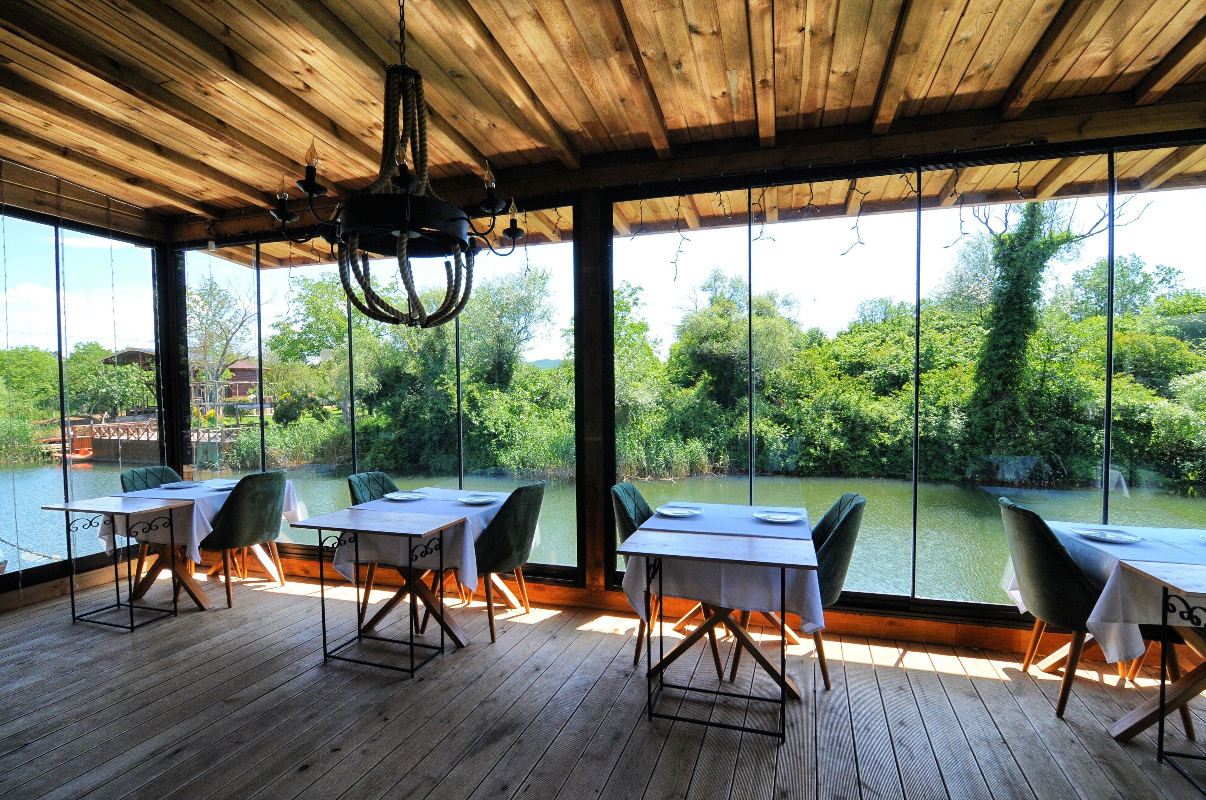 A dining area with tables and chairs, large windows, and a wooden ceiling.