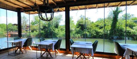 A dining area with tables and chairs, large windows, and a wooden ceiling.