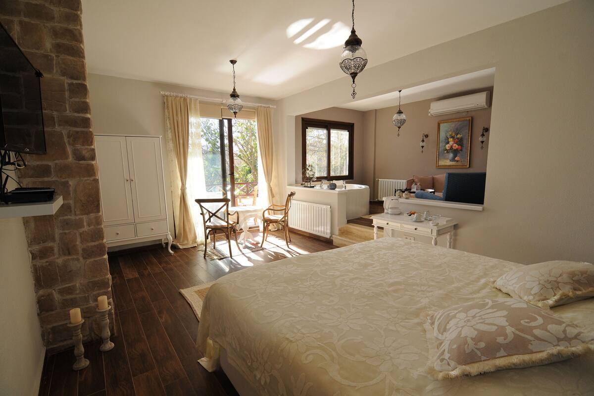 A bedroom with a large bed, a dresser, a vanity, and a window with curtains.