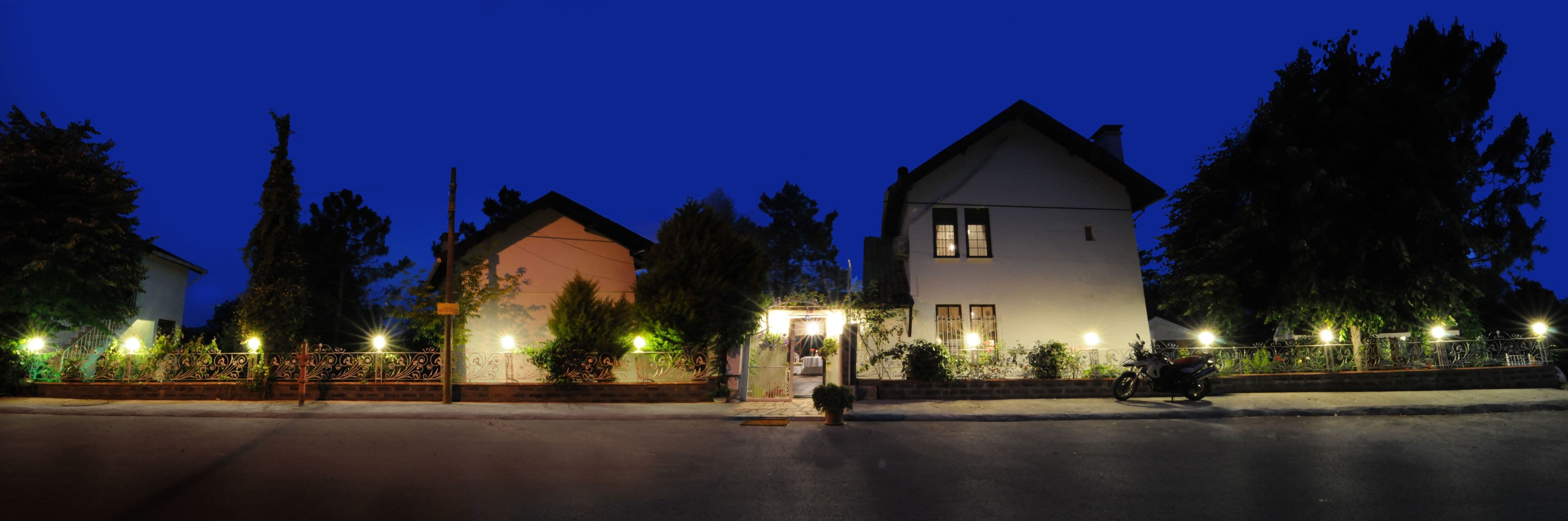 A two-story building with a gated entrance, a motorcycle parked in front, and a well-lit pathway.