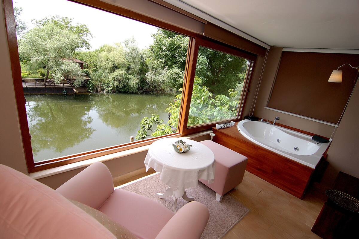 A room with a large window, a bathtub, and a small table with a decorative bowl.
