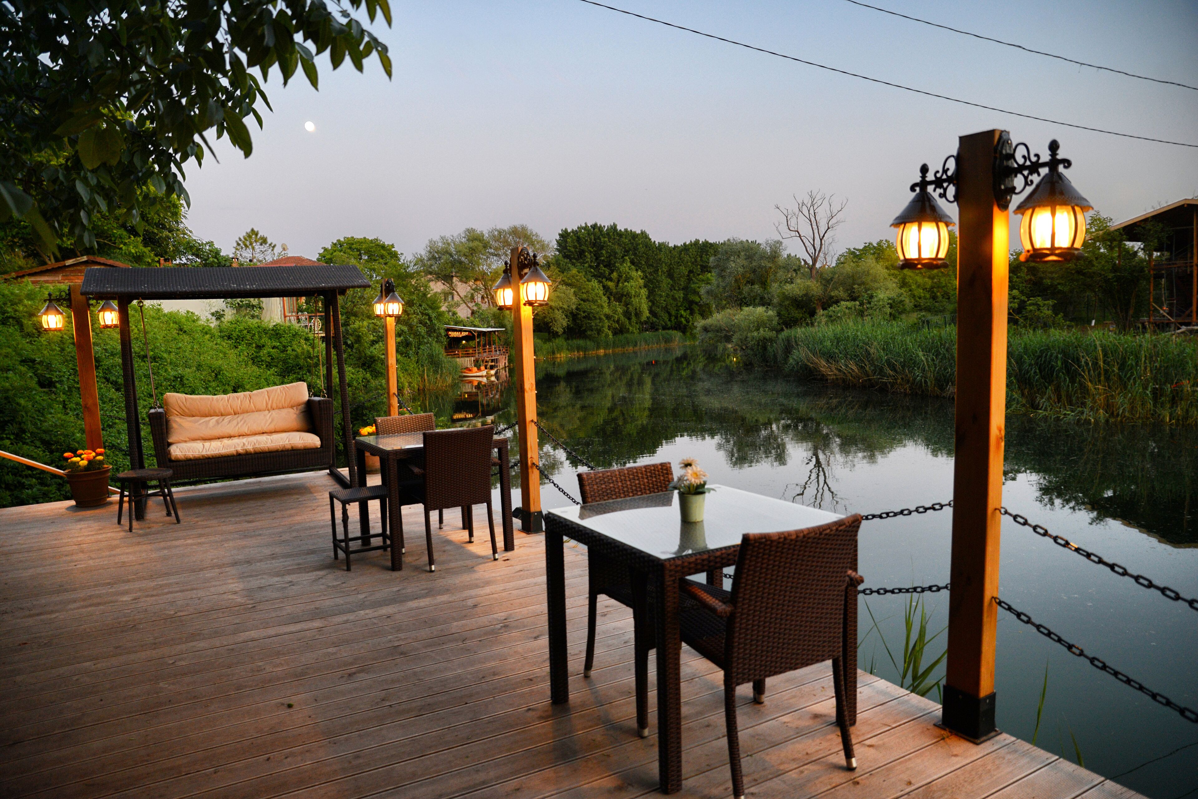 Eine Holzterrasse mit Tisch und Stühlen, umgeben von einem Teich und viel Grün.
