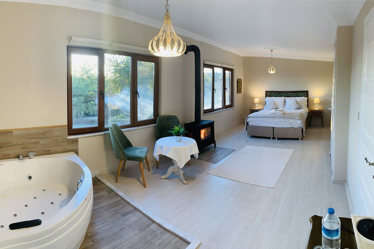A spacious room with a large bathtub, a cozy seating area with a table and chairs, a fireplace, and a bed with a nightstand.