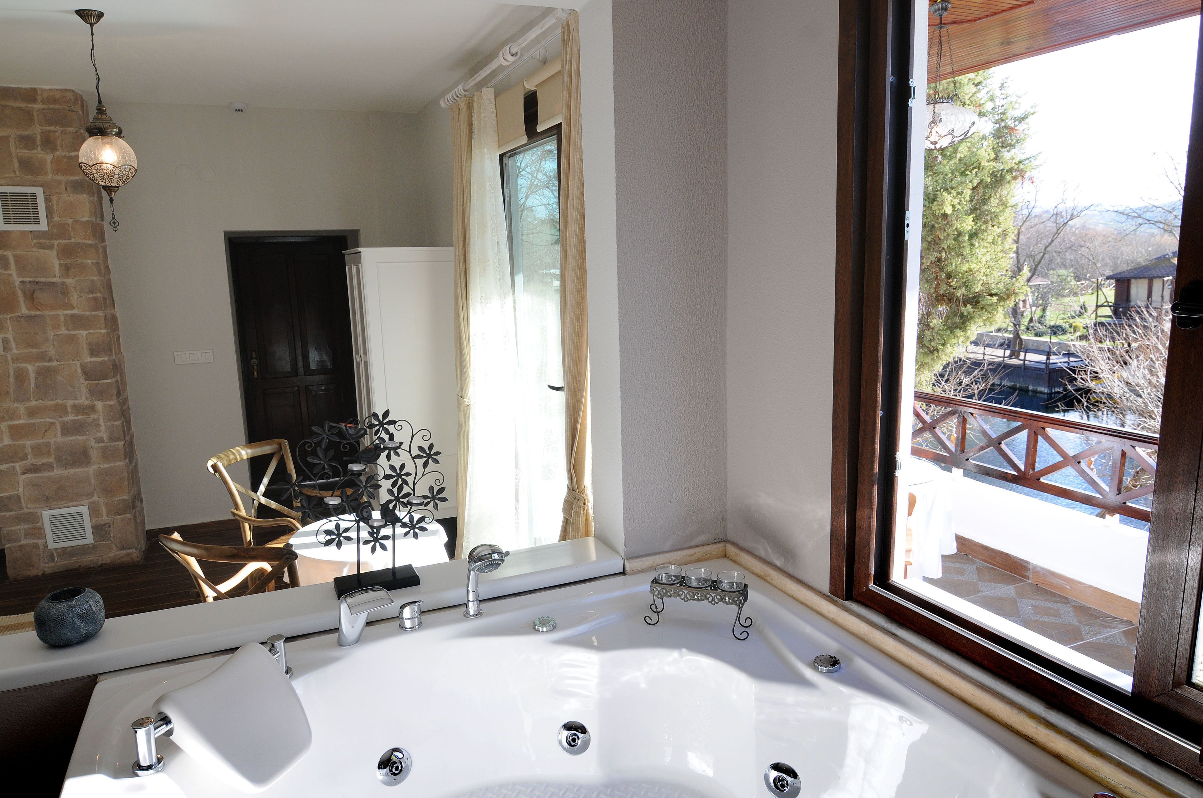 Een badkamer met een groot bad, een spiegel en een raam met uitzicht op een balkon.