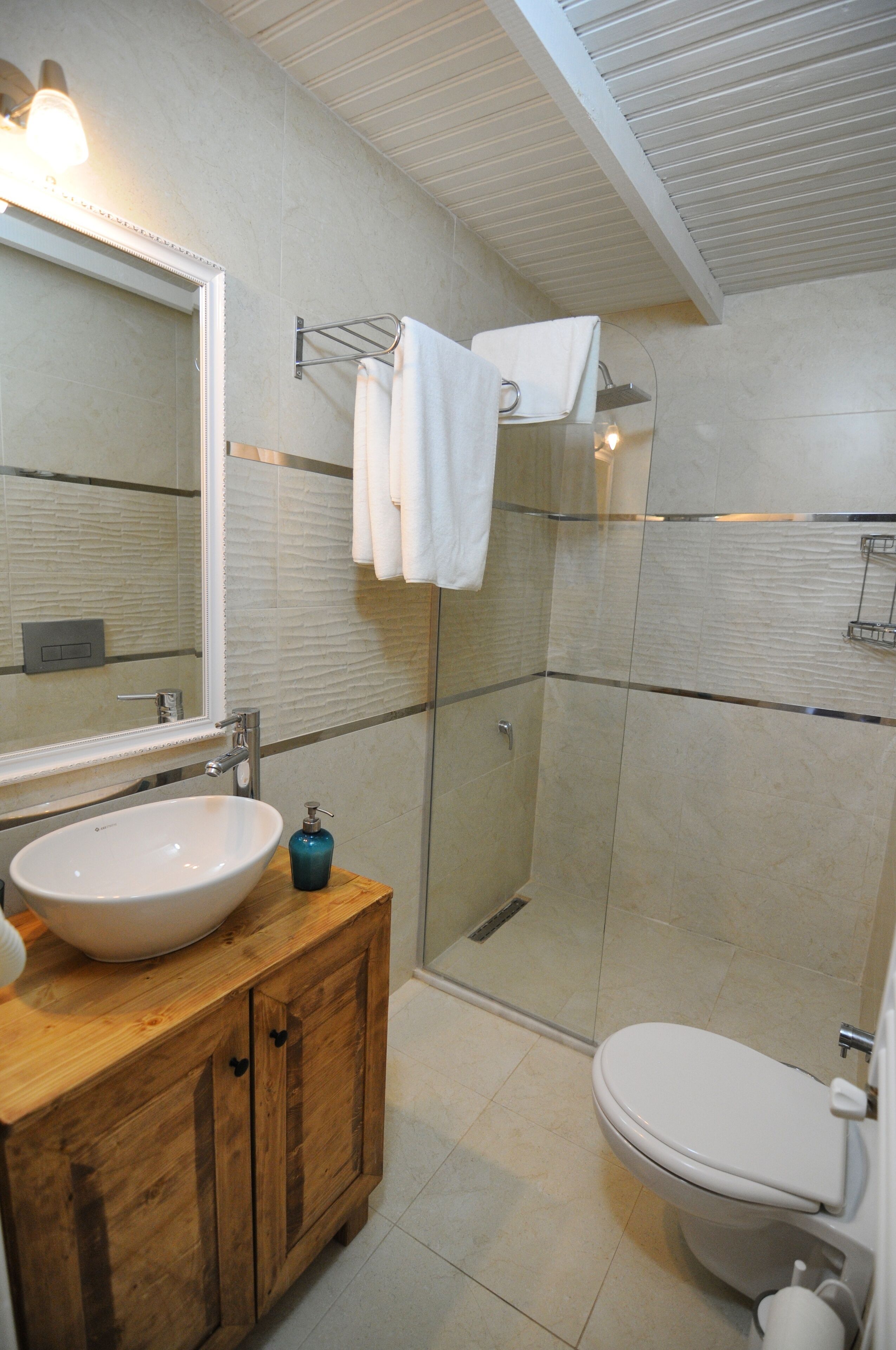 A modern bathroom with a large mirror, a wooden vanity, a white sink, a glass-enclosed shower, and a toilet.