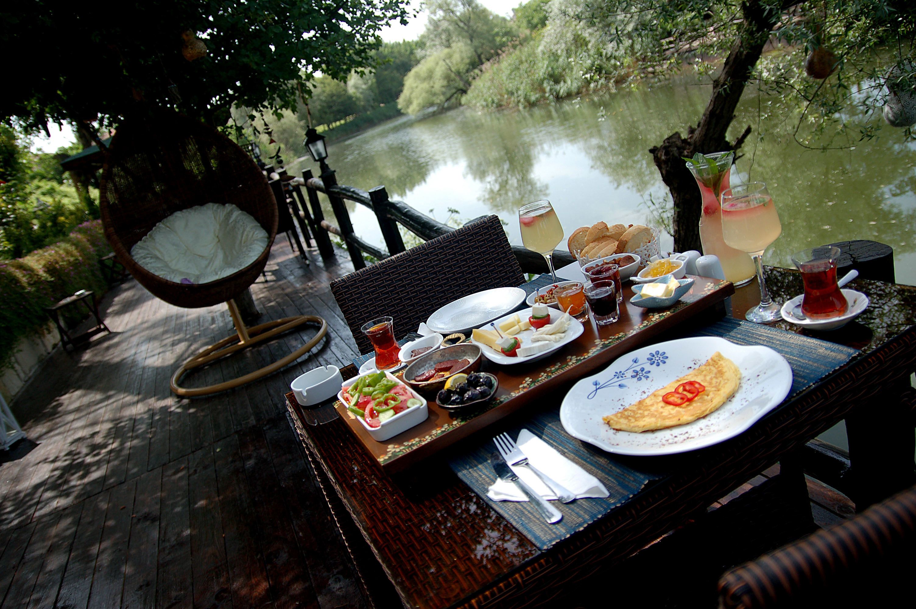 Una mesa de comedor con varios platos, una silla colgante y vista a un río.