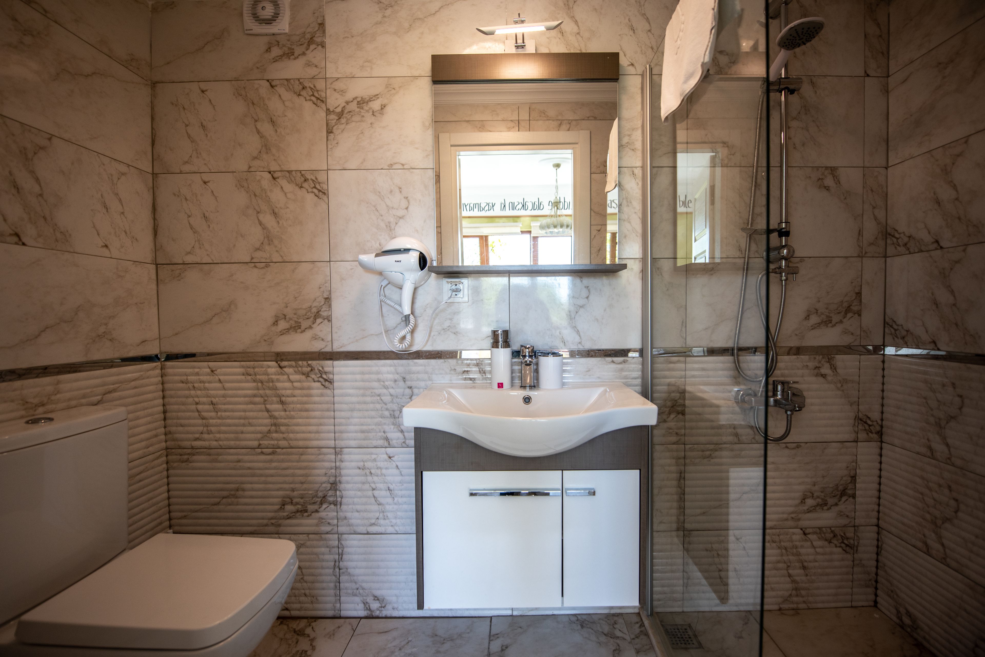 A modern bathroom with a marble floor, a white sink, a glass shower enclosure, and a toilet.