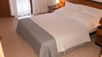 A hotel room with a bed, a nightstand with a lamp, and a window with curtains.