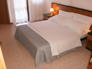 Una habitación de hotel con una cama, una mesita de noche con lámpara y una ventana con cortinas.