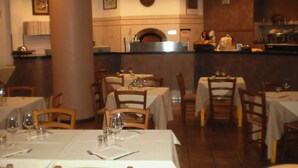 A restaurant interior with tables set for dining, a kitchen area, and a wall-mounted clock. - RTA Le Corti (Grosseto)