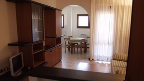 A living room with a dining table and chairs, a sofa, and a TV on a stand. - RTA Le Corti (Grosseto)
