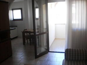 Un interior amb una porta corredissa de vidre que dona a un balcó, una zona de menjador amb taula i cadires, i un sofà.
