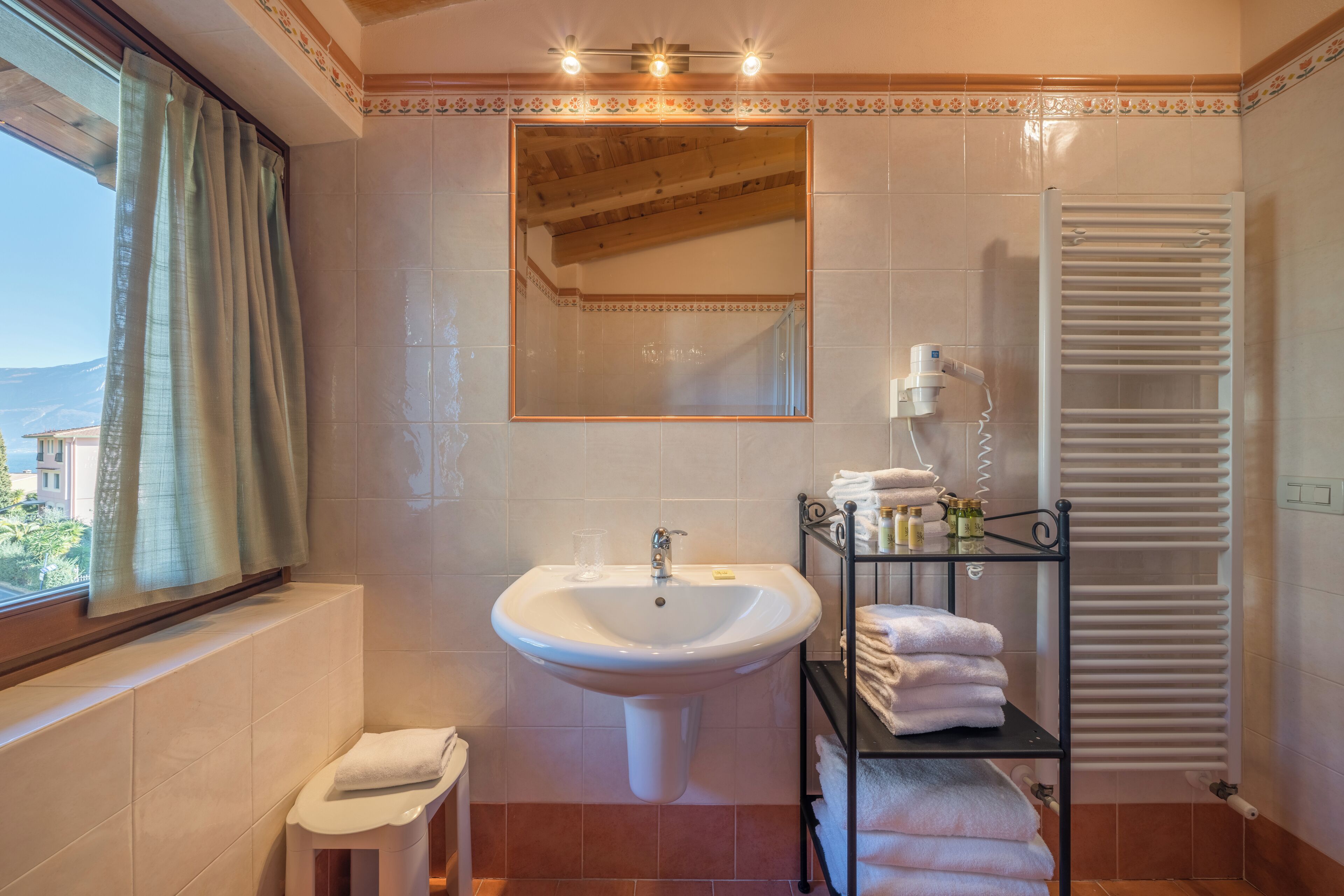 A bathroom with a sink, mirror, towel rack, and window with curtains.
