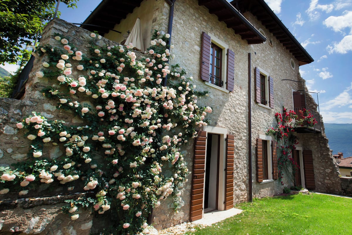 Une maison en pierre avec un jardin, un balcon fleuri et une vue sur la mer.