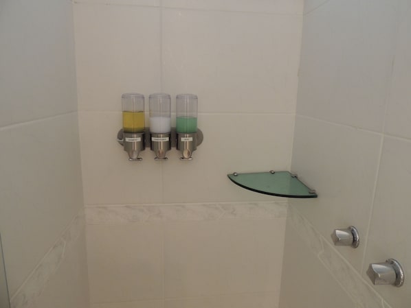 A bathroom with three dispensers for shampoo, conditioner, and soap.