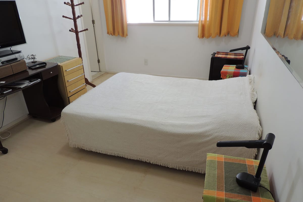 Une chambre à coucher avec un lit, un bureau, une chaise, une lampe et une fenêtre avec des rideaux.