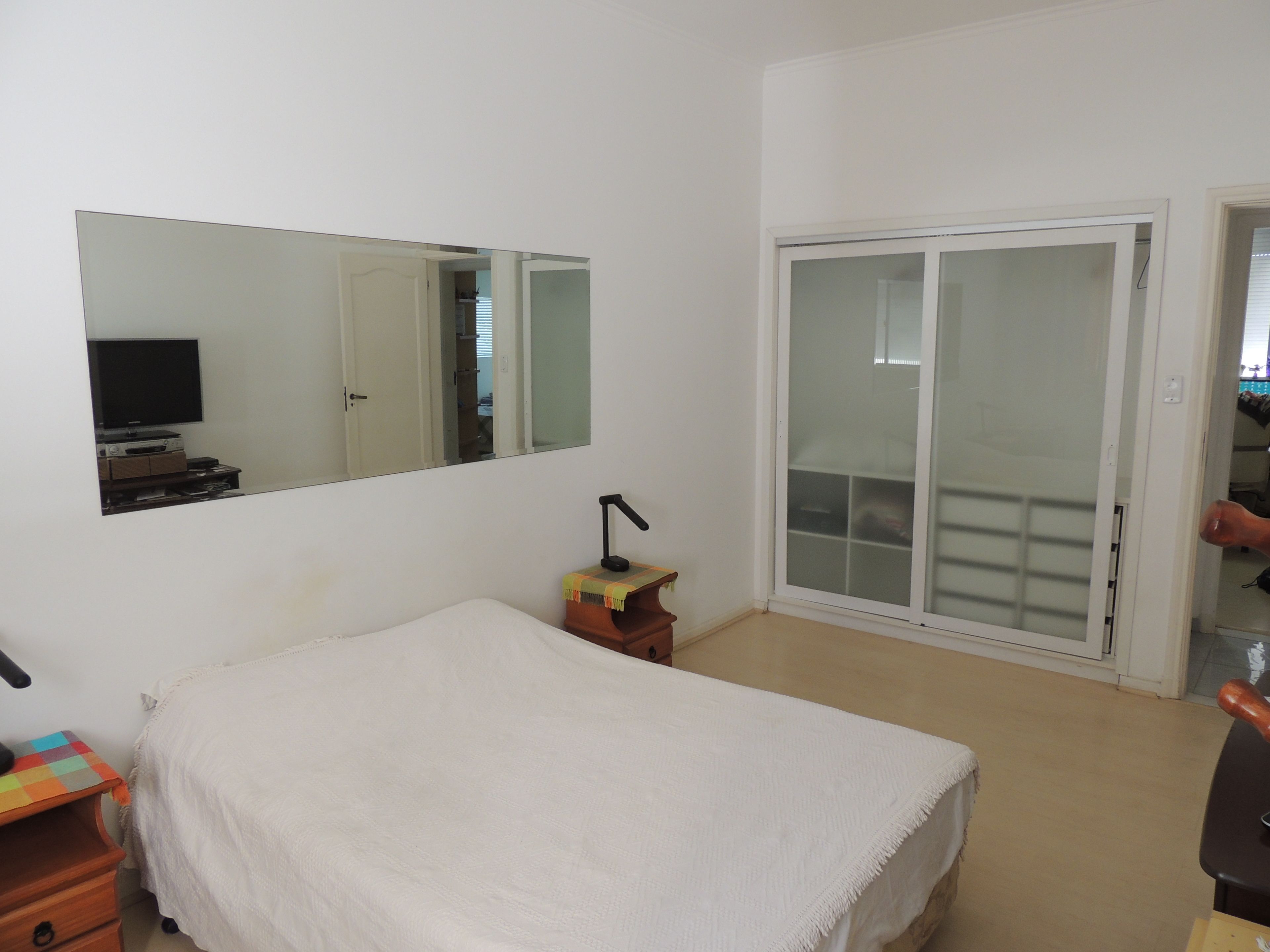 Une chambre à coucher comprenant un lit, un bureau, une chaise, un miroir et une porte-fenêtre coulissante donnant sur un balcon.