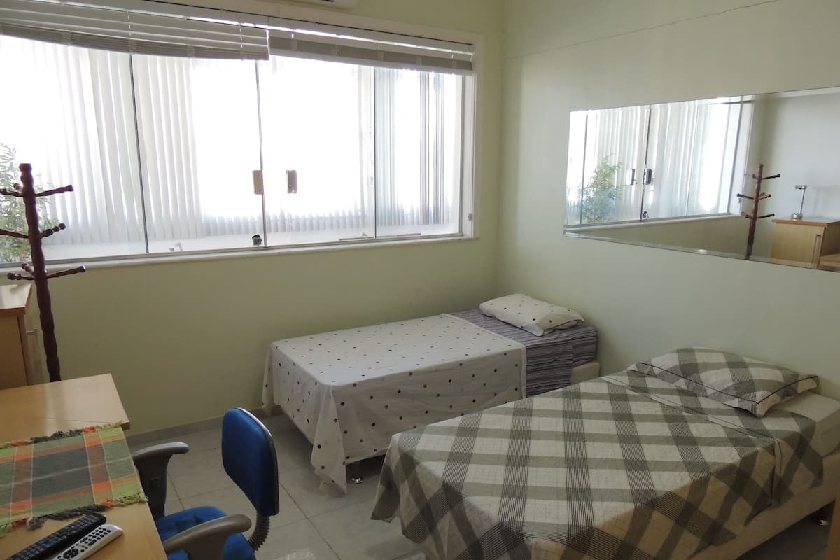 Une petite pièce propre, avec un lit, un bureau, une chaise et une fenêtre équipée de stores.