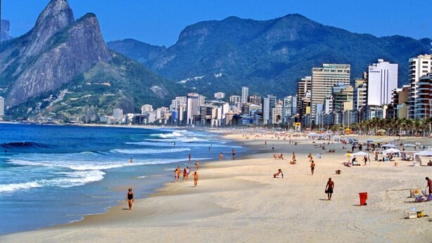Una playa con gente, una montaña y edificios al fondo.