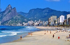 A beach with people, a mountain, and buildings in the background.