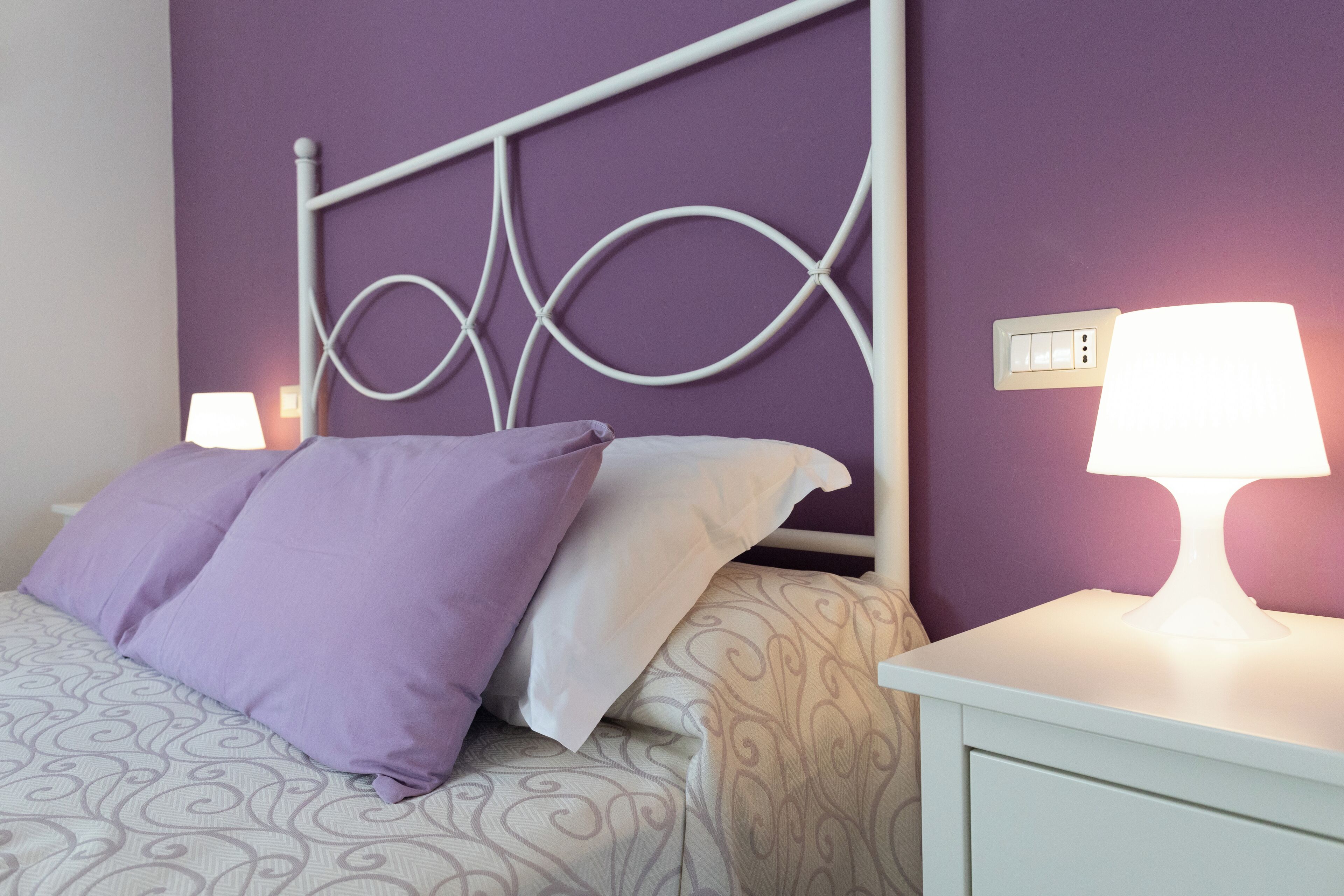 A neatly made bed with patterned bedding, a white metal headboard, and a bedside table with a lamp.