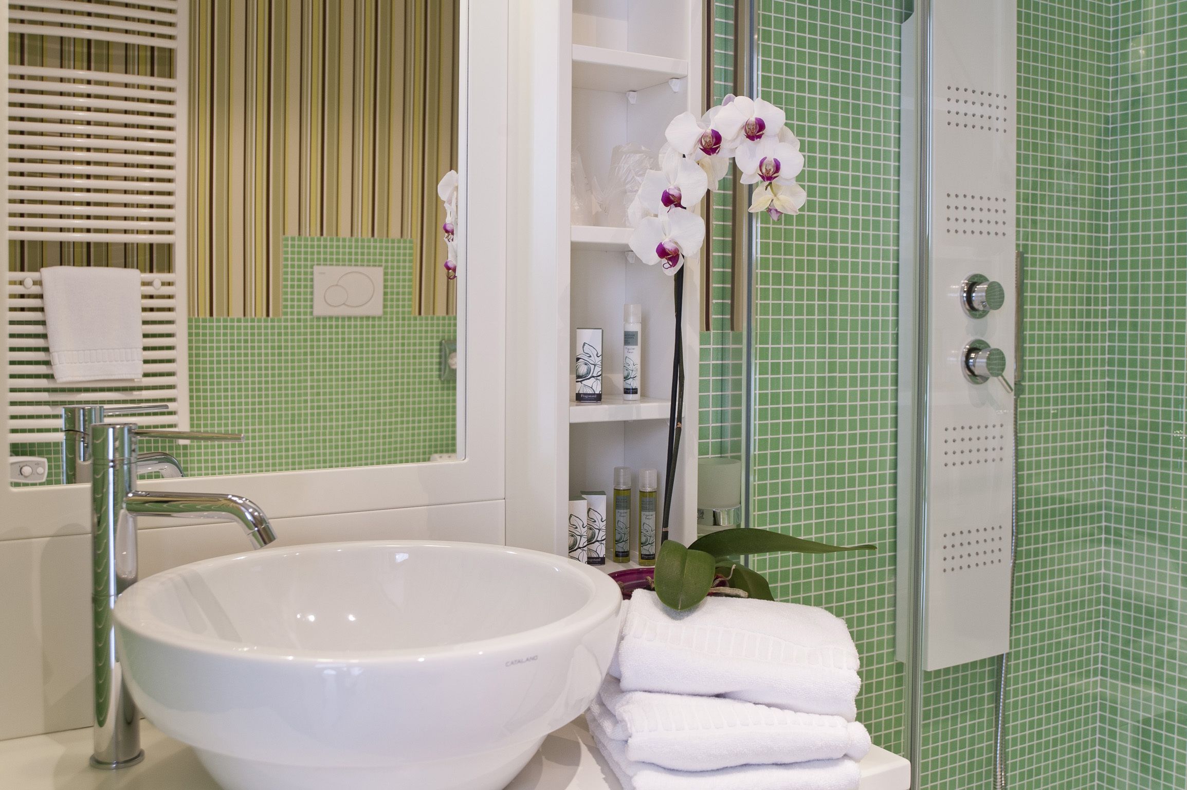 Ein Badezimmer mit weißem Waschbecken, einem Spiegel, einer Dusche und grünen Fliesen.
