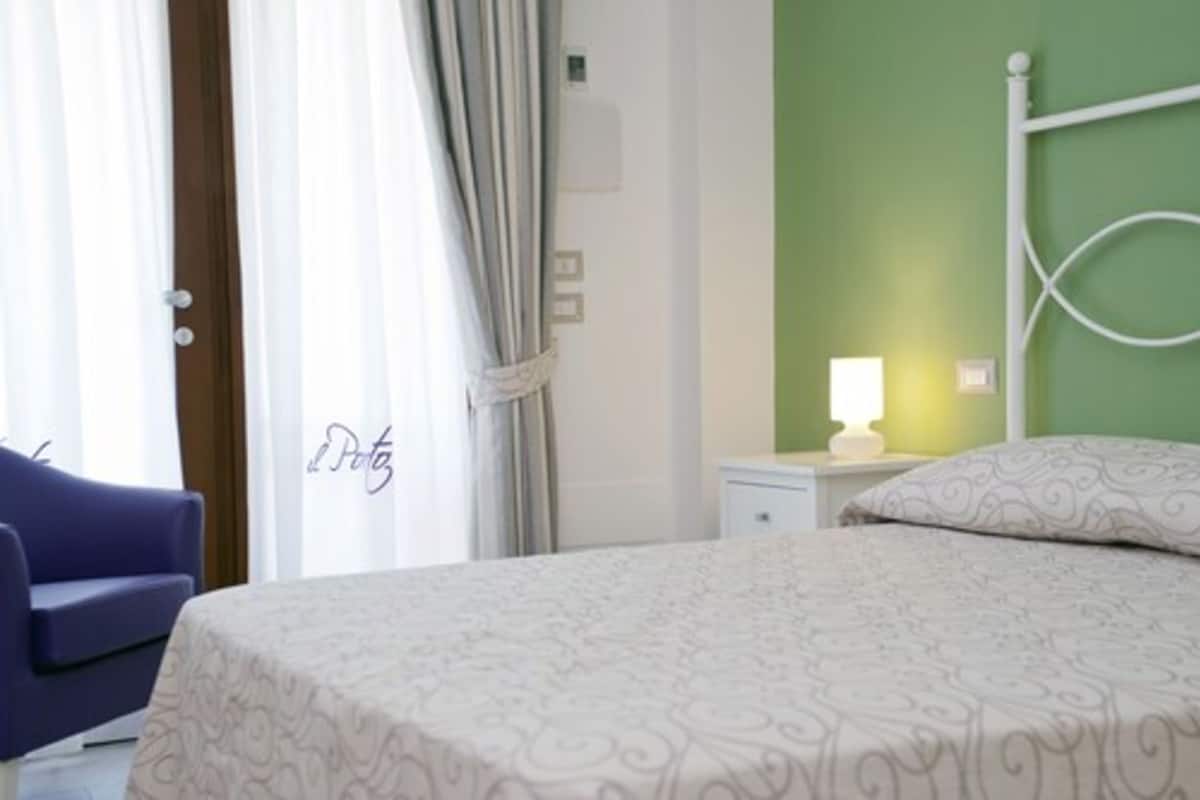 Ein Hotelzimmer mit einem Bett, einem Nachttisch mit Lampe, einem Sessel und Vorhängen.