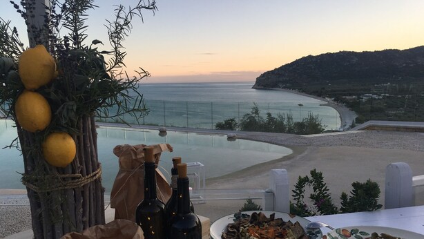 A table with bottles, a plate of olives, and a scenic view of the sea at sunset. - Hotel Residence Il Porto (Mattinata)