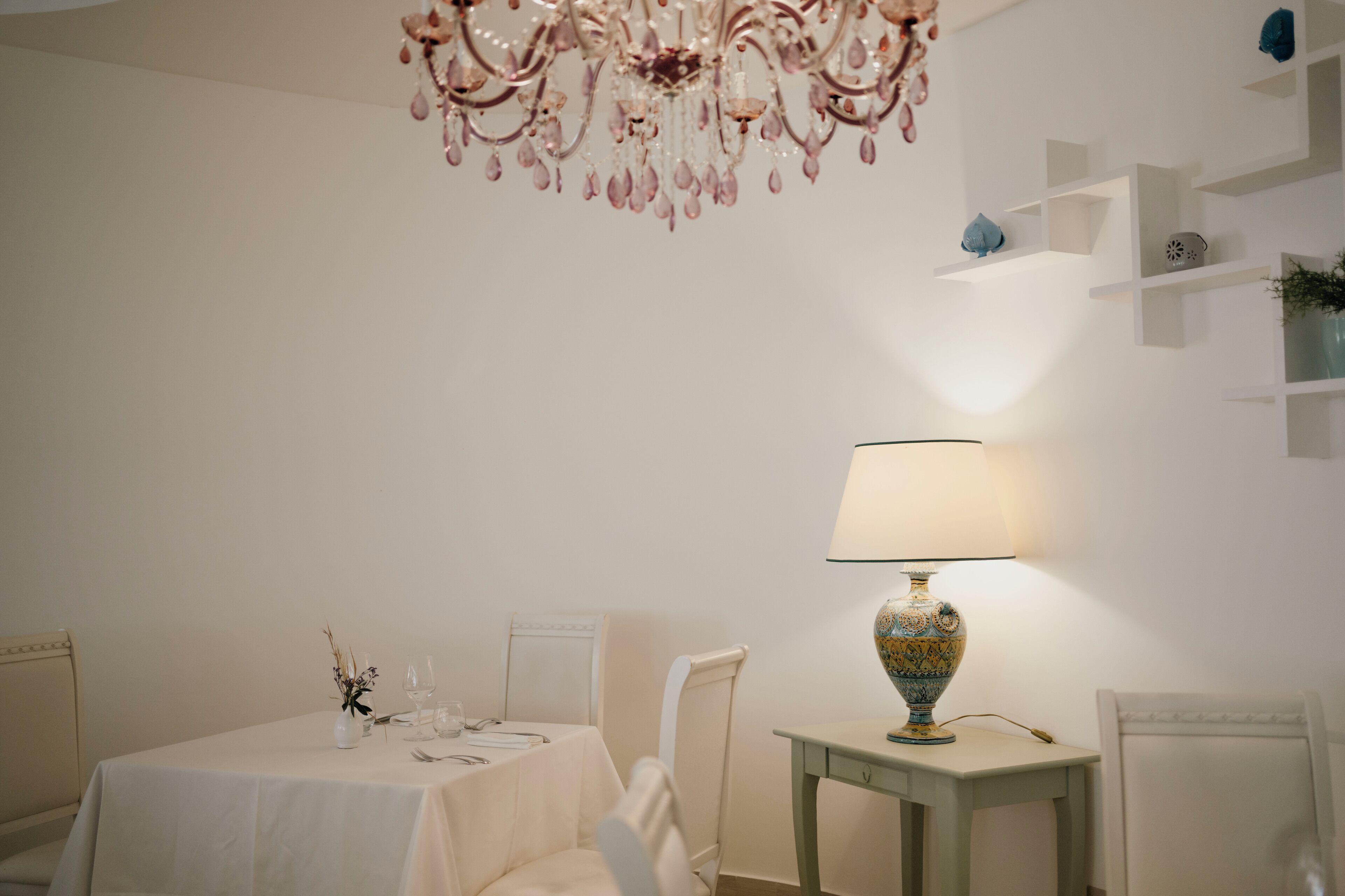 A dining area with a table set for two, a chandelier, and a lamp on a side table.
