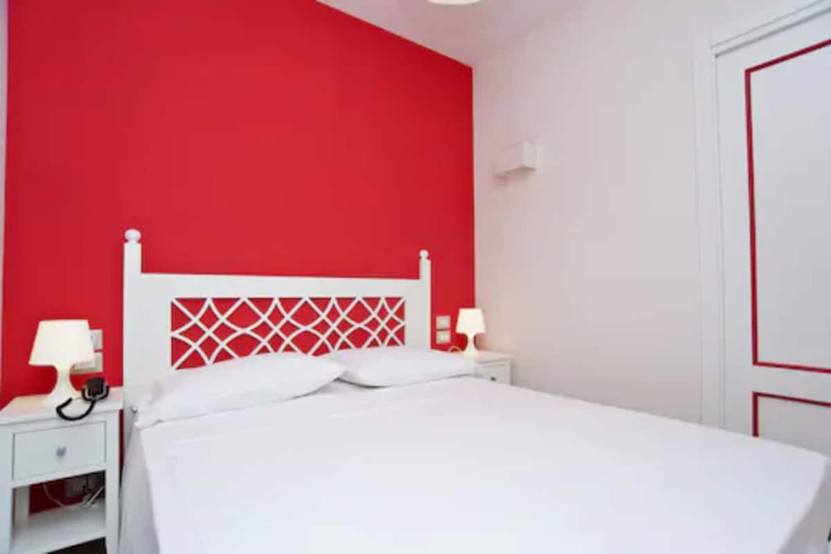 Ein Schlafzimmer mit einem weißen Bett, roten Wänden und einem weißen Kopfende mit einem geometrischen Muster.