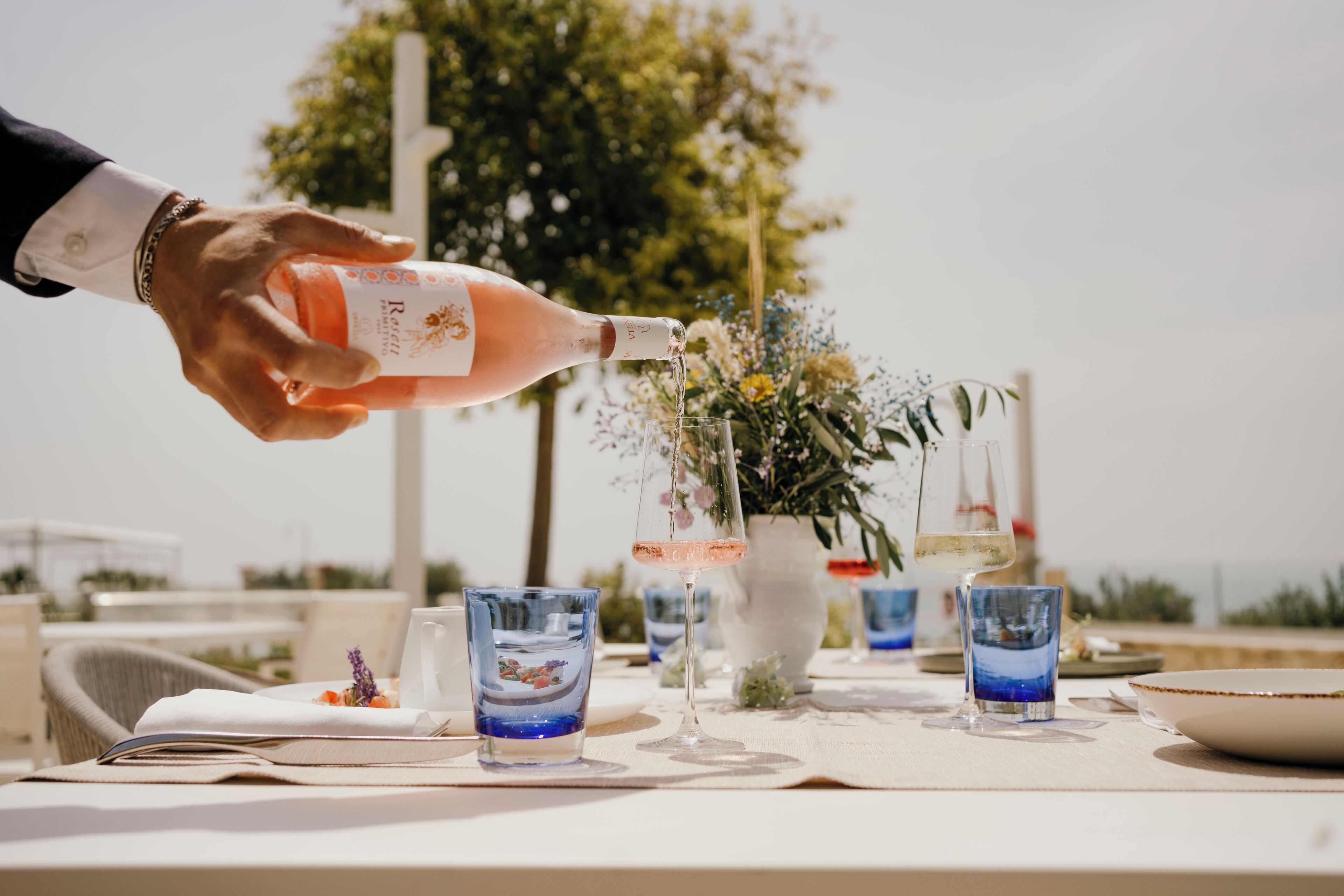 Une table mise pour un repas, avec une bouteille de vin dont on verse le contenu dans un verre.
