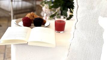 Un rincón acogedor para leer con un banco acolchado, un libro, un plato de cruasanes y un vaso de jugo de cereza.