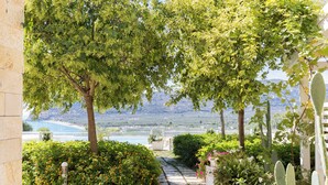 A garden pathway leading to a scenic view with a body of water and mountains in the background. - Hotel Residence Il Porto (Mattinata)
