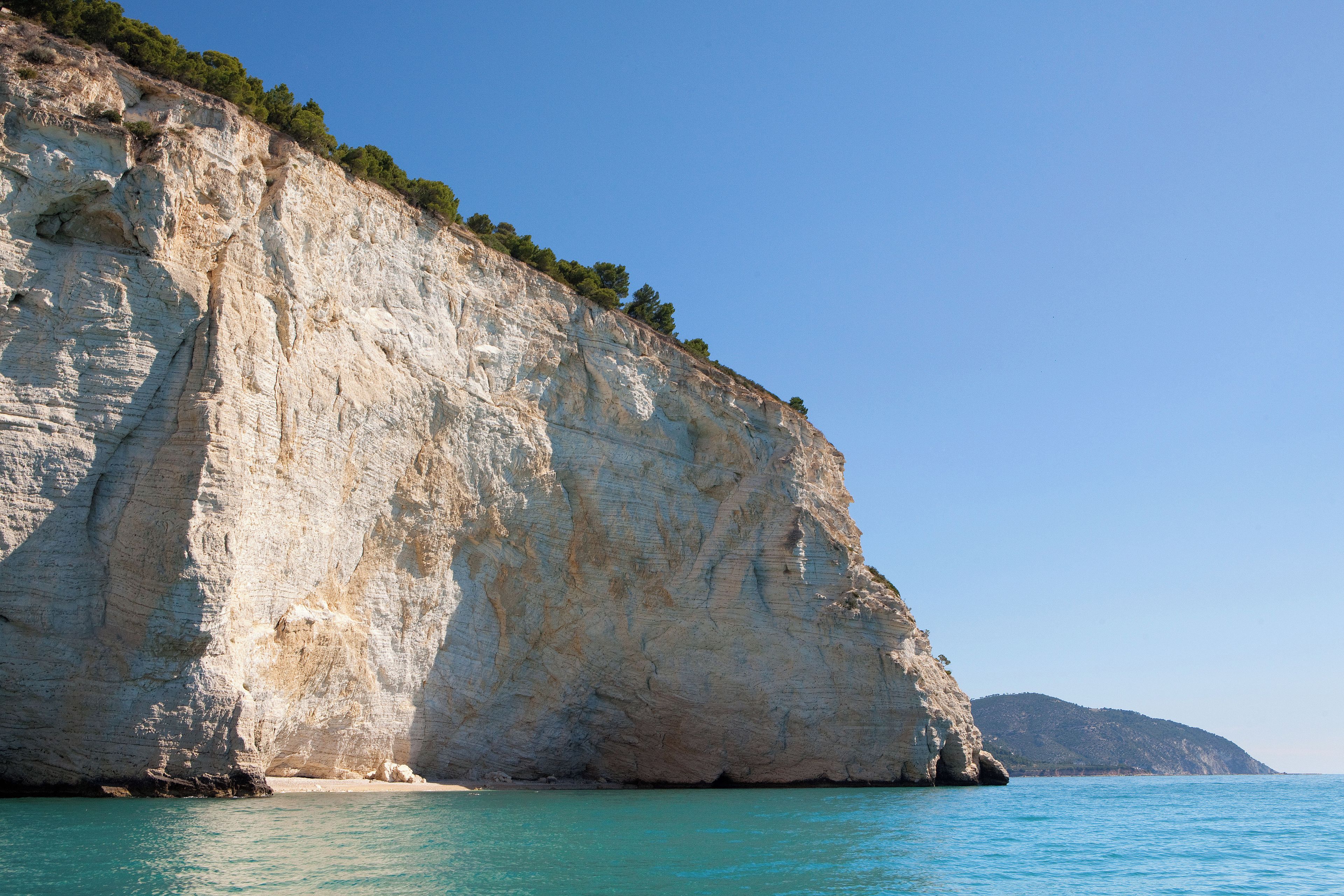 A coastal cliff with a clear view of the sea and a distant mountain.