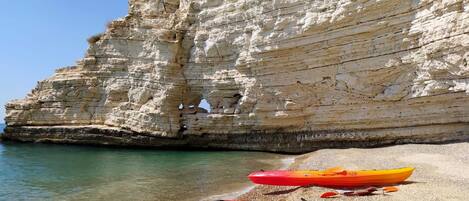 Kayaks sobre una playa de guijarros con aguas claras y acantilados blancos al fondo.