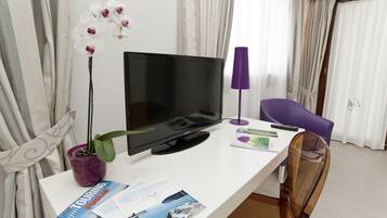 Ein Hotelzimmer mit Flachbildfernseher, einem violetten Sessel, einem Topf mit einer Orchidee und einer Zeitschrift auf dem Tisch.