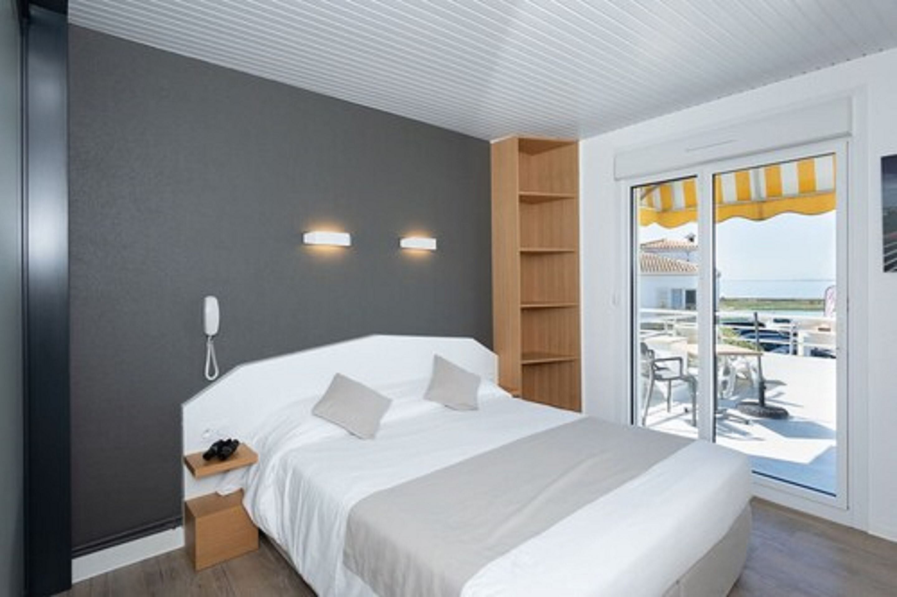 Ein modernes Hotelzimmer mit einem großen Bett, einem Nachttischtelefon und Blick auf den Außenbereich durch eine Schiebetür.