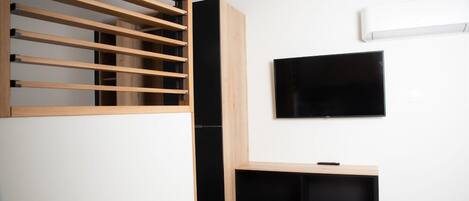 Ein modernes Wohnzimmer mit an der Wand montiertem Fernseher, einer Holz-Lamellen-Raumtrennung und einer eingebauten Bank.