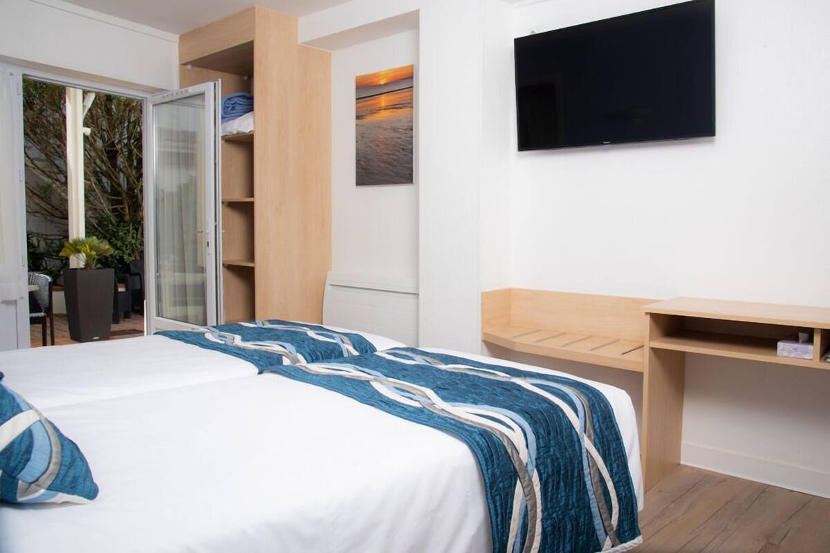 Une chambre à coucher comprenant un lit, un téléviseur fixé au mur, un bureau en bois et une porte coulissante donnant sur un espace extérieur.