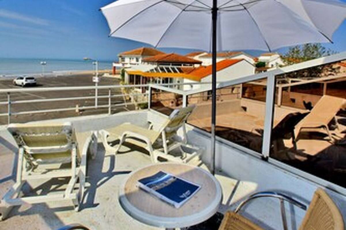 Un balcon avec des sièges d’extérieur, une table et un grand parasol.