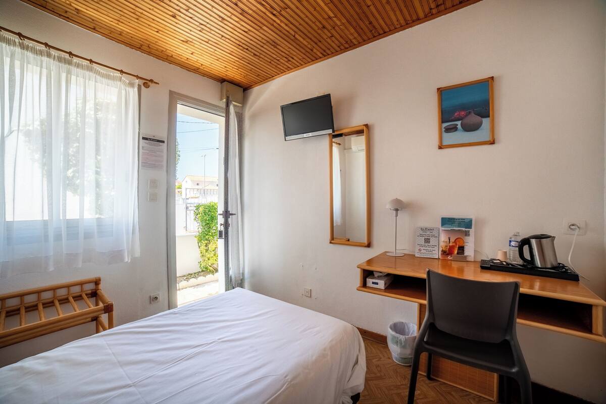 Une chambre d’hôtel comprenant un lit, un bureau avec une chaise, une télévision, un miroir et une fenêtre avec des rideaux.