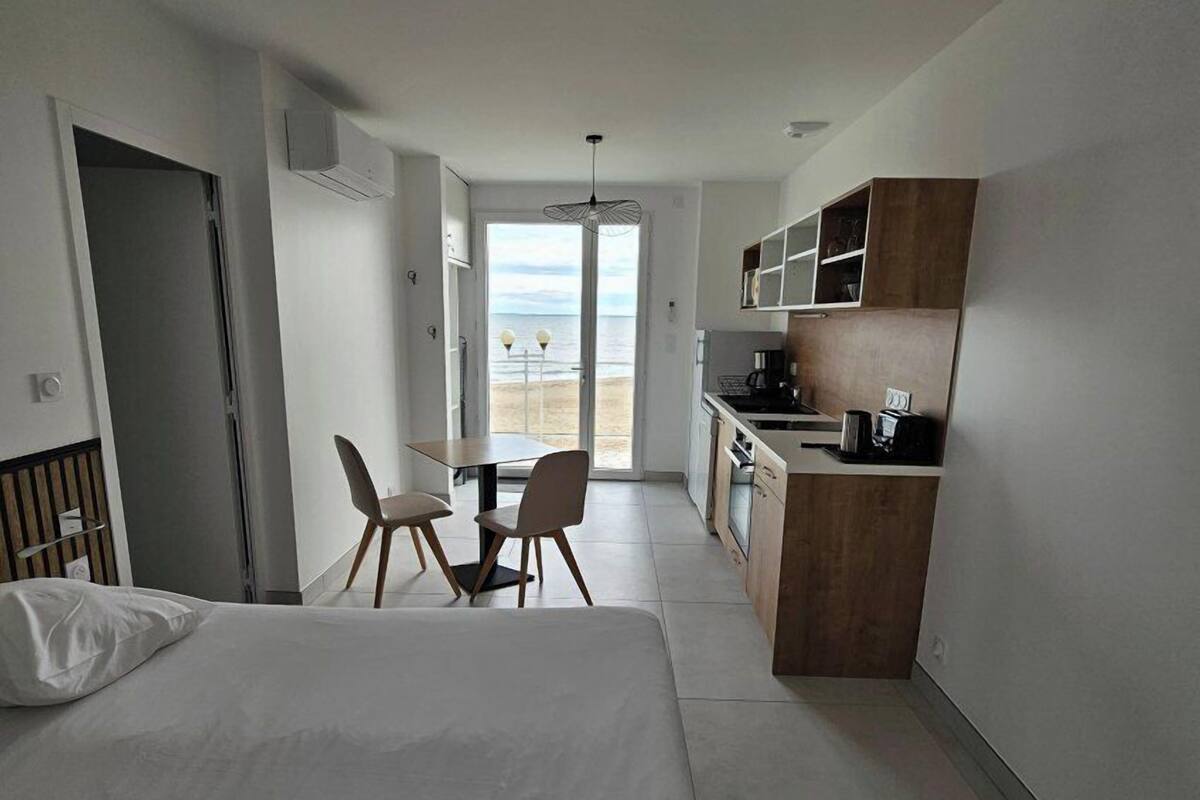 Une chambre d’hôtel moderne équipée d’un lit, d’une table à manger avec des chaises, d’un coin cuisine et offrant une vue sur la plage.