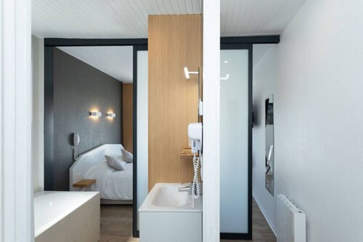 Une chambre d’hôtel moderne équipée d’un lit, d’une table de chevet et d’une salle de bain avec un lavabo et un miroir.